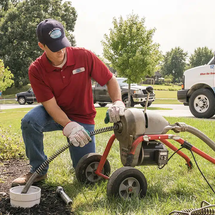 Reid & Pederson technician using a Ridgid K-1500 sewer machine to perform outdoor drain cleaning in Crete, IL. A branded company van is parked in the background, highlighting their professional sewer and drain services.