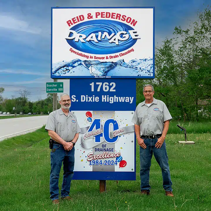 Two Reid & Pederson Drainage team members standing in front of the company’s sign at 1762 S. Dixie Highway, Crete, IL, celebrating 40 years of drainage excellence from 1984 to 2024.
